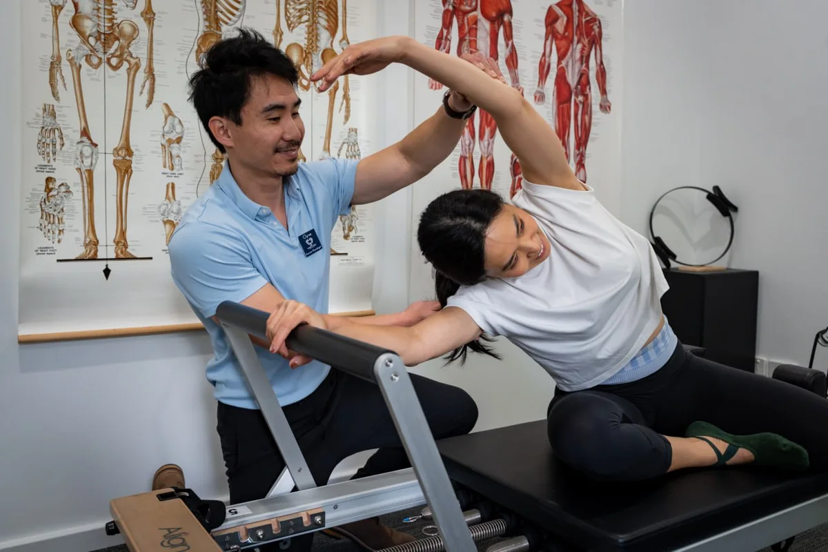 Clyve Tan guiding a patient through a clinical Pilates exercise on the reformer
